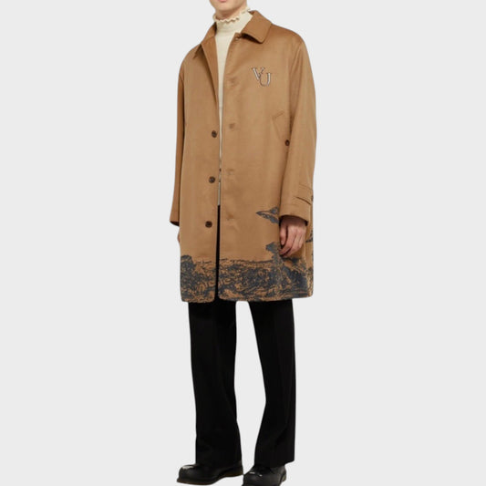 Tasoni beige cashmere coat with grey UFO embroidery and a landscape print on the hem. Model wears a cream turtleneck and black trousers.