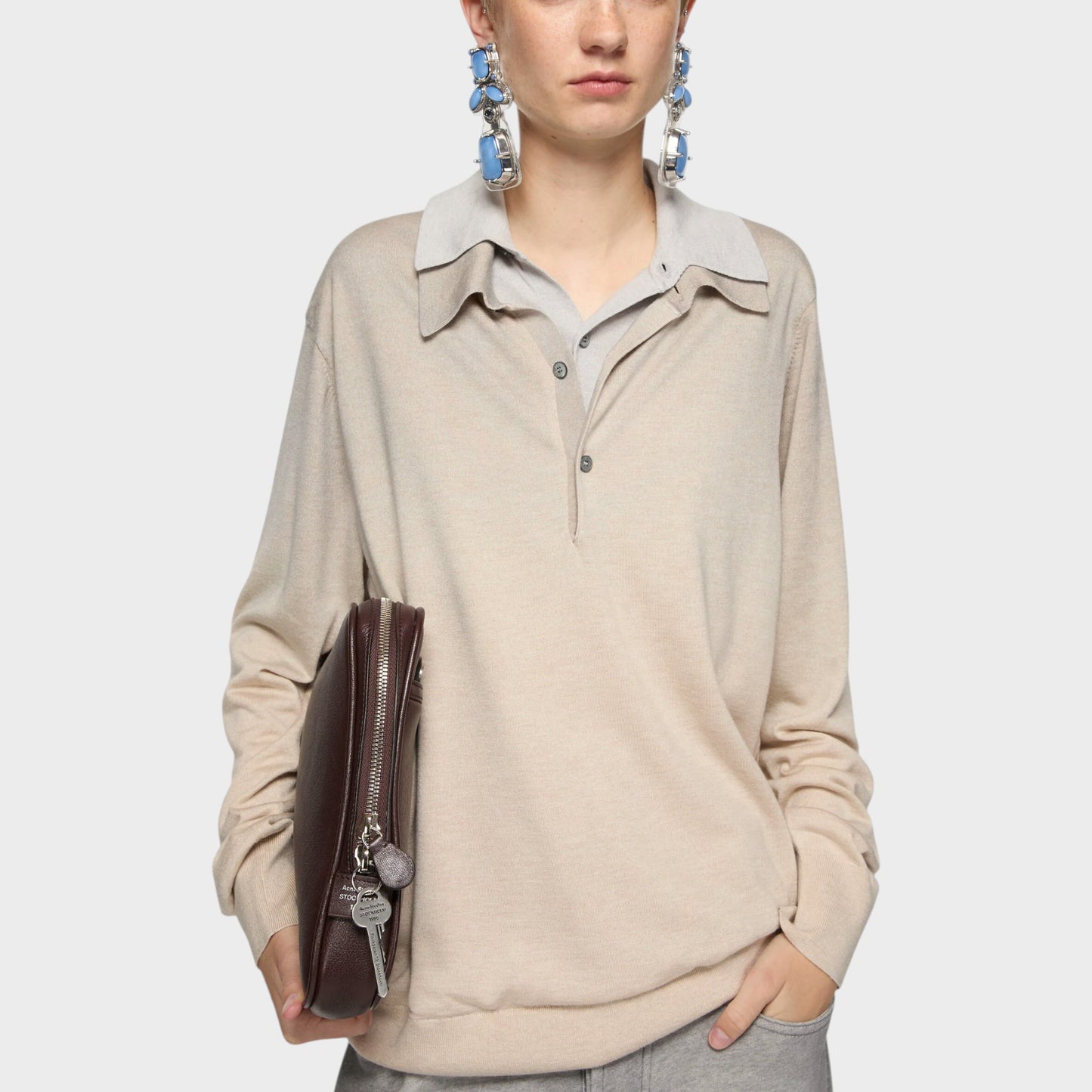Tasoni beige silk and cashmere layered V-neck sweater with grey collar and cuffs. Model holds a brown leather clutch.