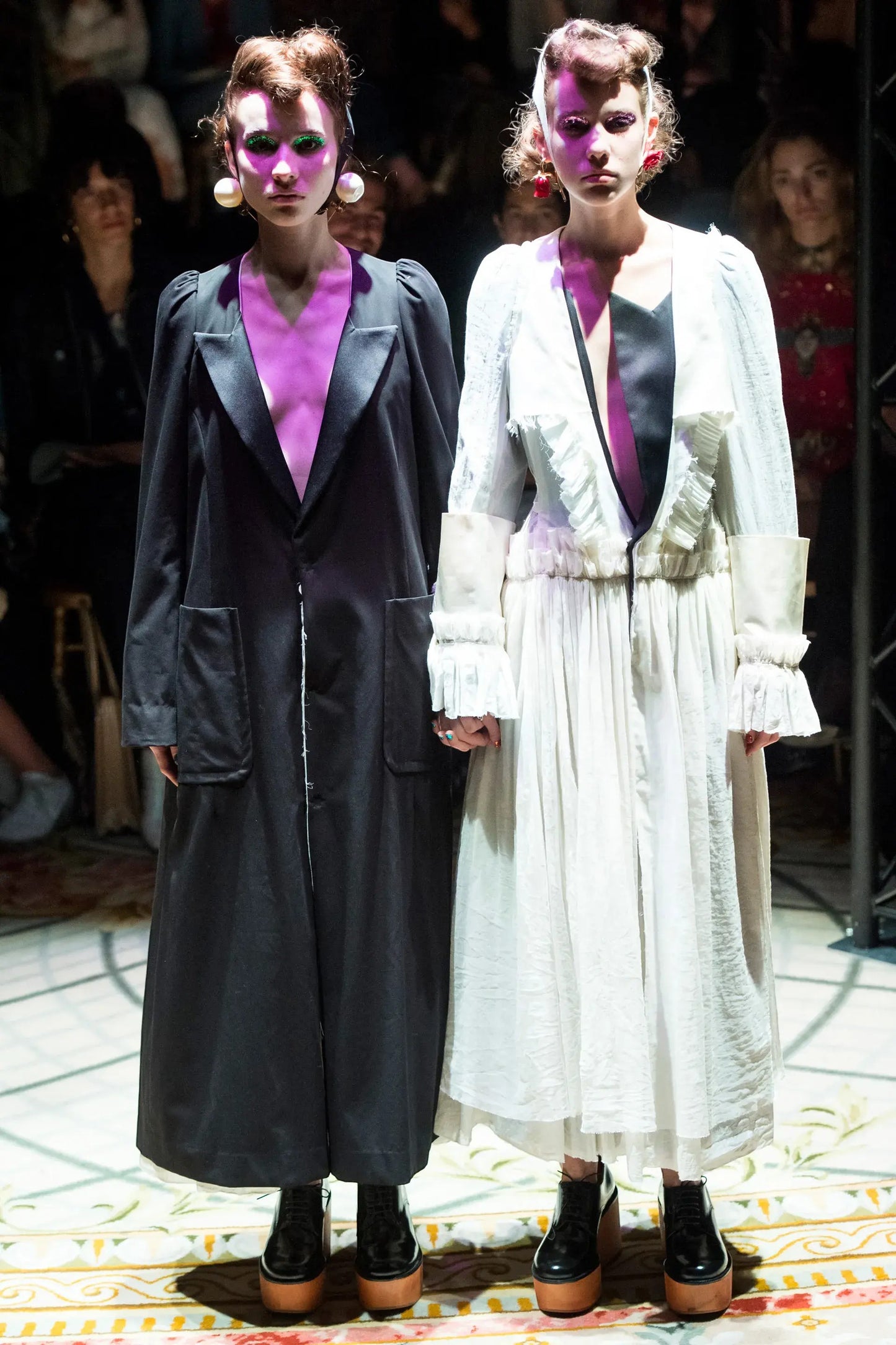 Tasoni black long coat with white ruffled lining and white long dress with ruffled details, worn by models on a runway.