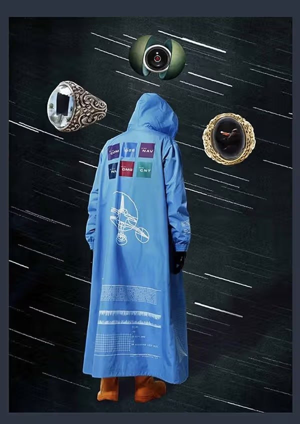 Tasoni sky blue hooded rain parka with graphic prints on the back and sleeves. Features a long silhouette and orange boots.