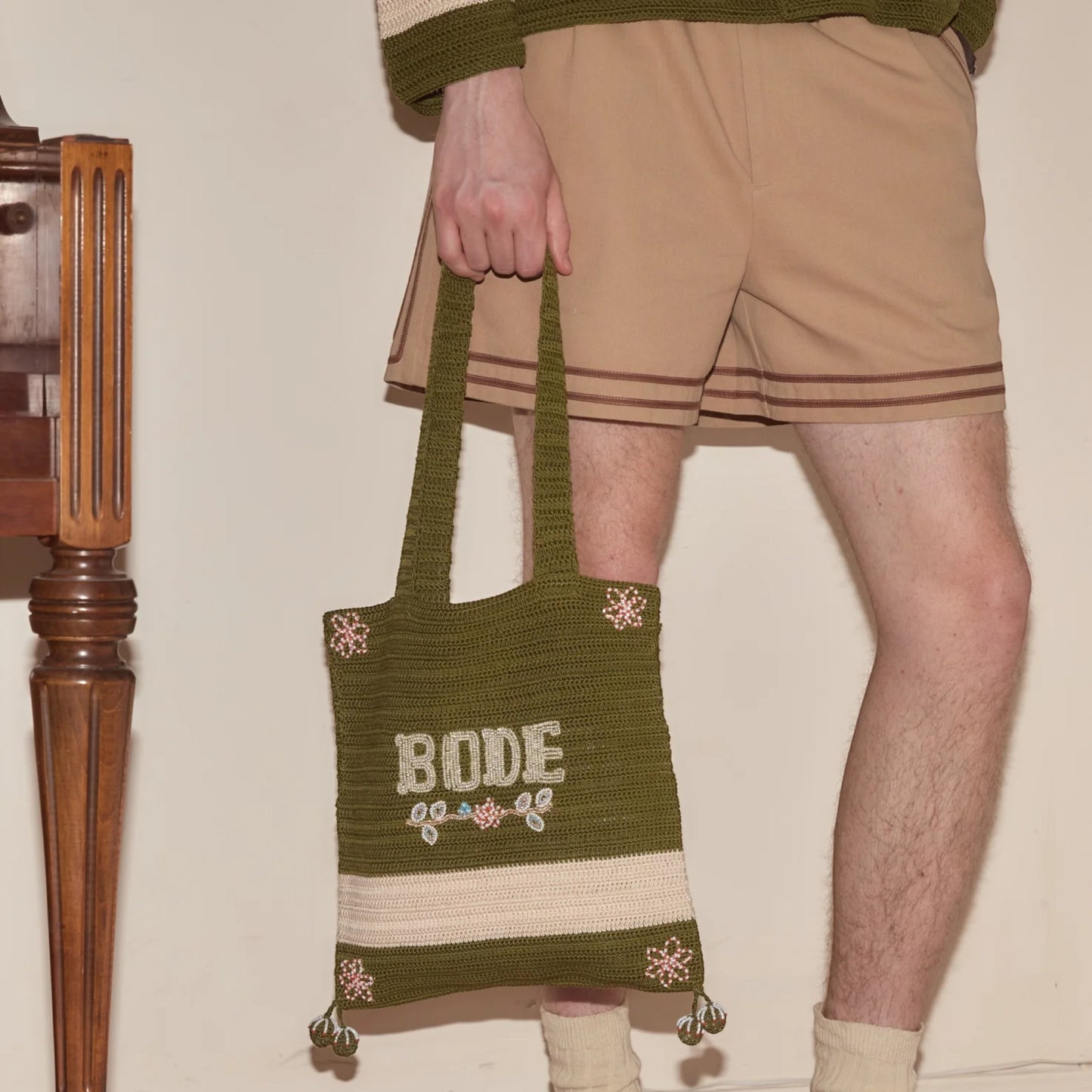 Tasoni Bode Marsh crochet tote bag in green yarn with cream stripe and beaded floral details. Features dual handles and open top.
