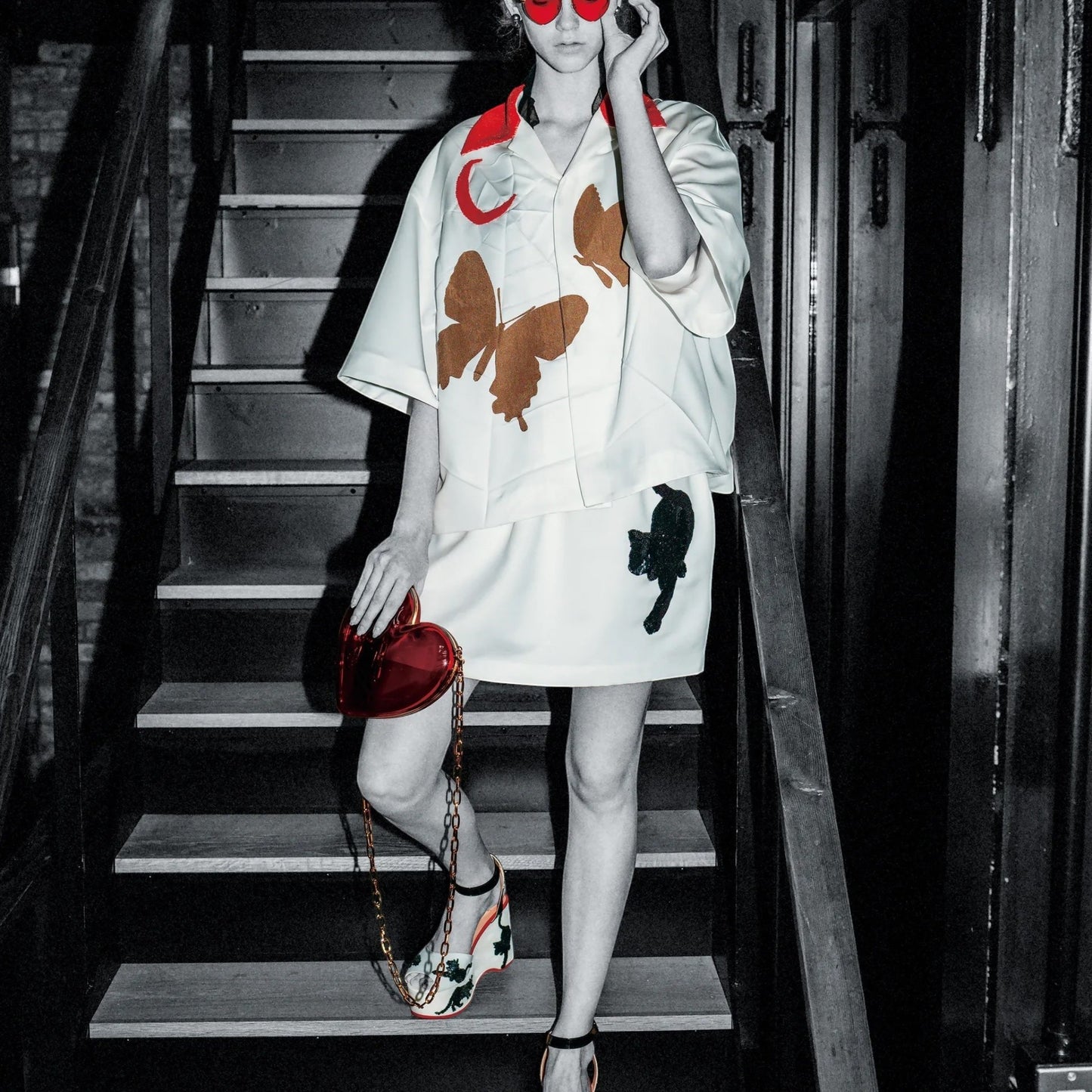 Tasoni white oversized short sleeve shirt with red collar, featuring brown butterfly and red moon motifs. Model wears heart-shaped sunglasses.