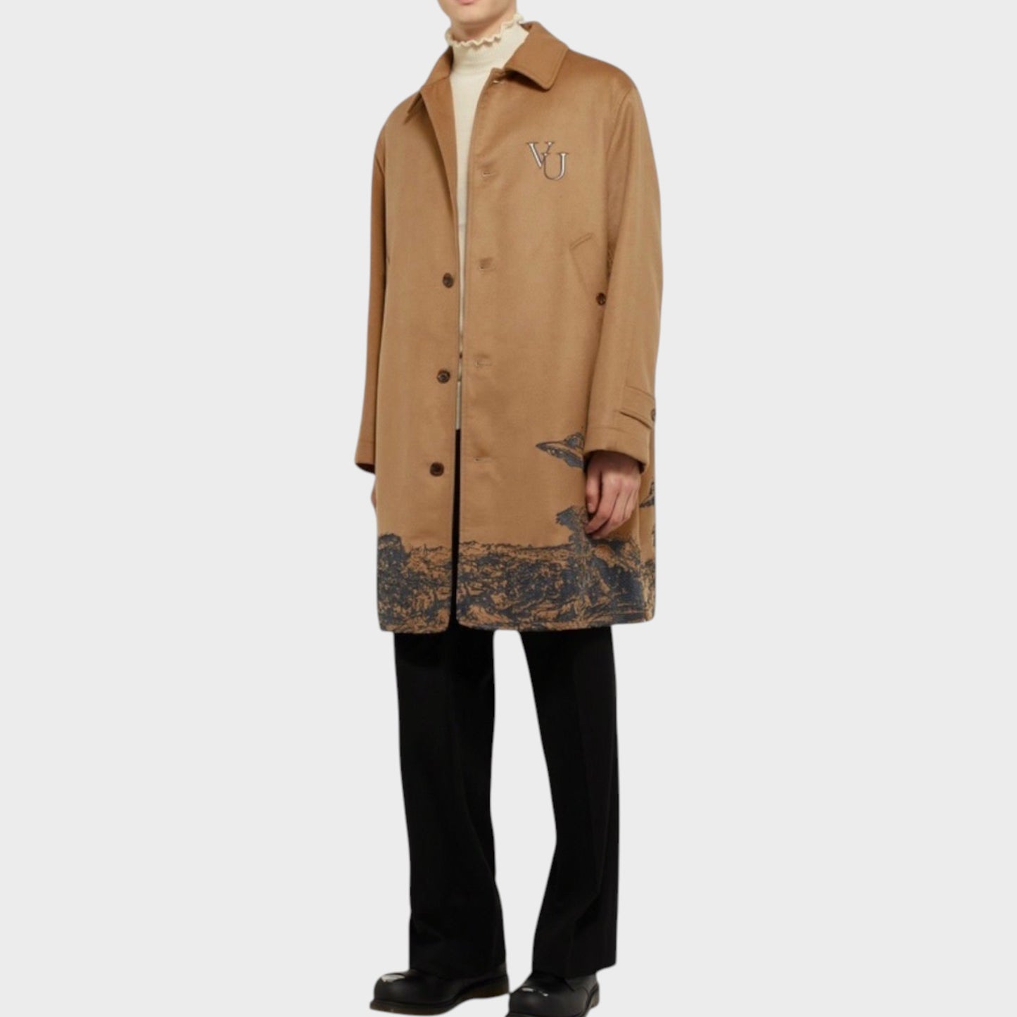 Tasoni beige cashmere coat with grey UFO embroidery and a landscape print on the hem. Model wears a cream turtleneck and black trousers.