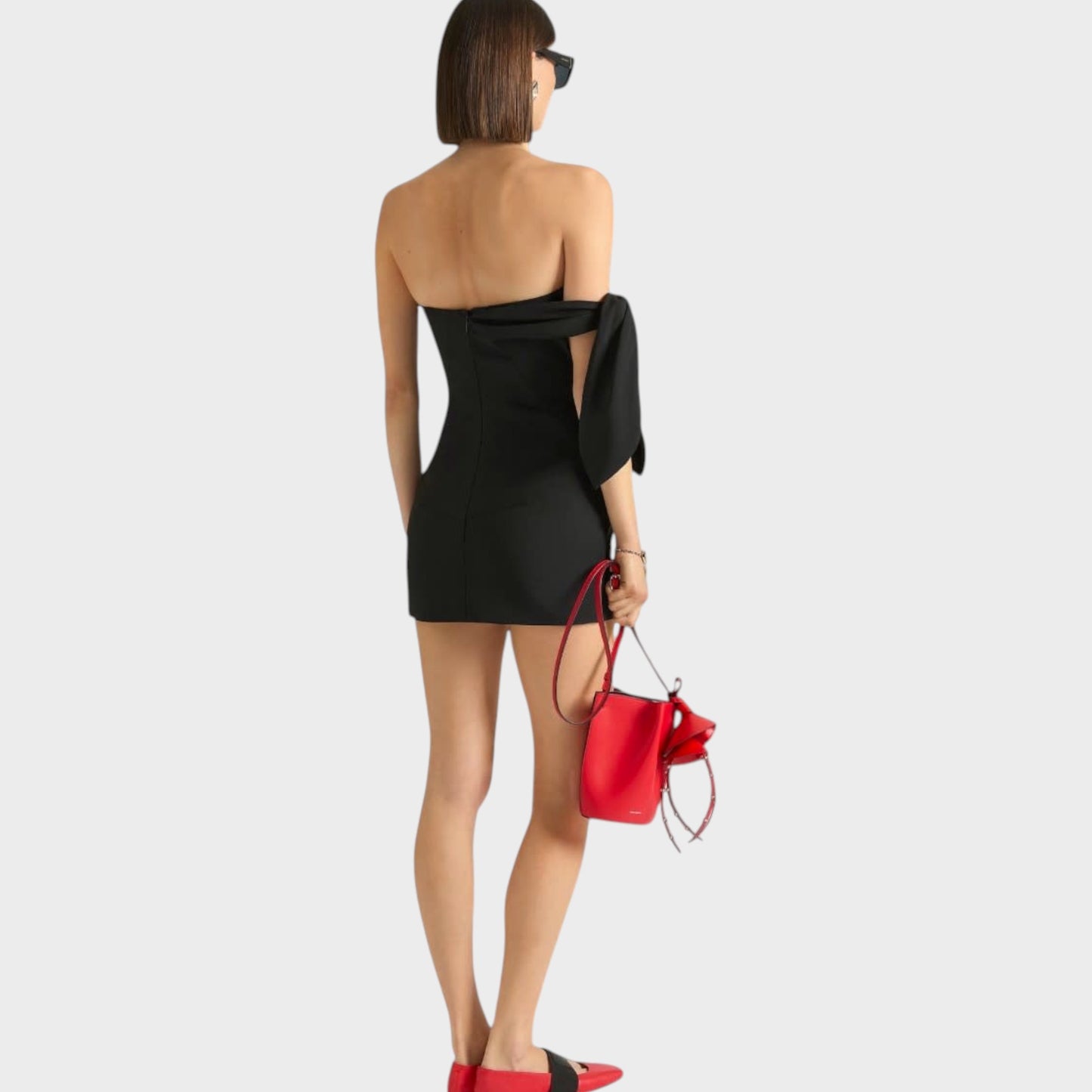 Tasoni black wool and mohair bustier mini dress with bow detail on shoulder, worn by a model with sunglasses and red accessories.