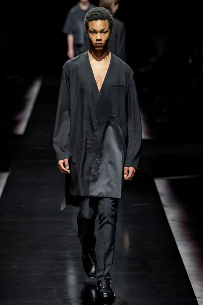 Tasoni black wool coat with asymmetric collarless design and Dracula motive print, worn by a male model on a runway.