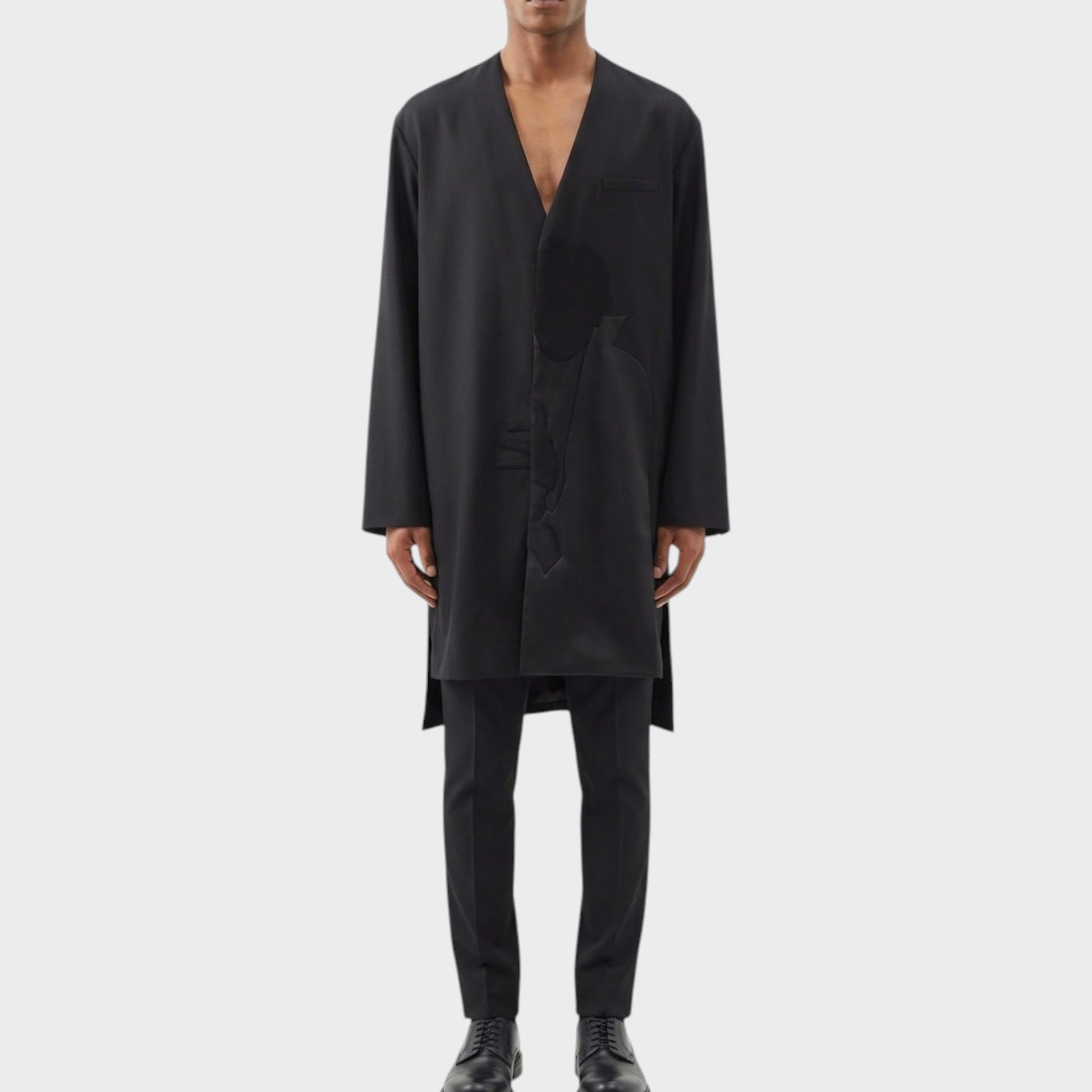 Tasoni black wool asymmetric collarless coat with Dracula motif, worn by a male model with black trousers and shoes.