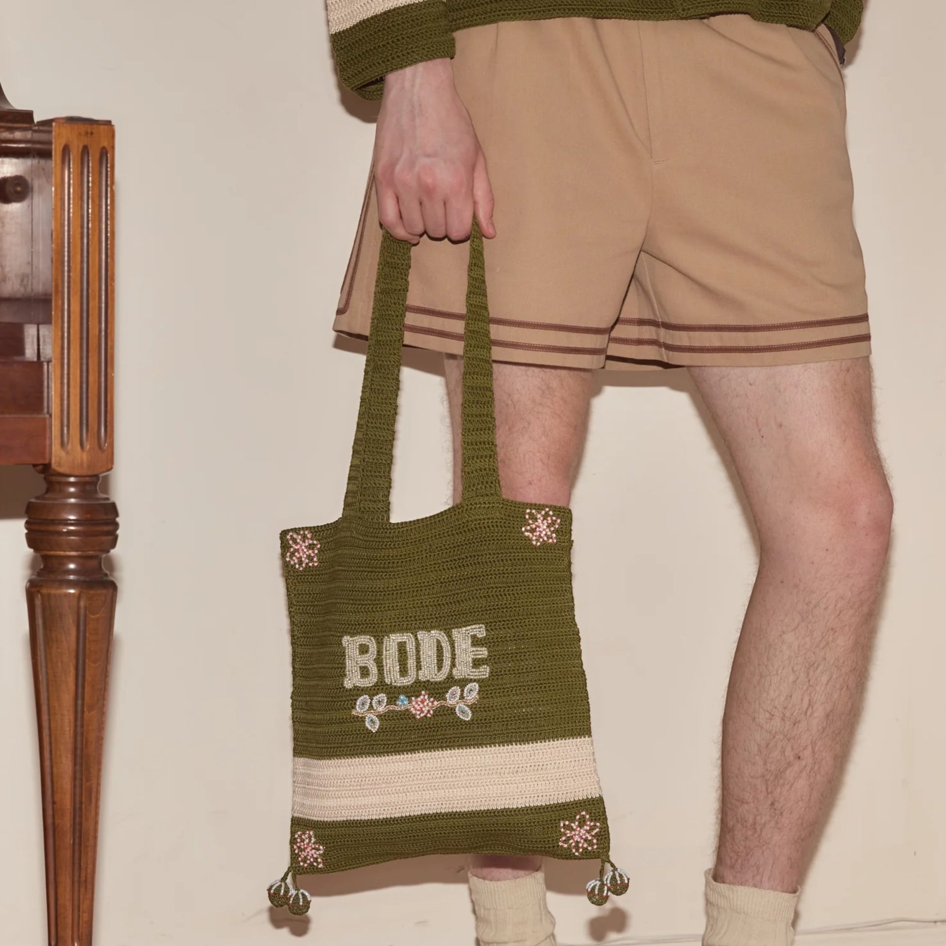 Tasoni Bode Marsh crochet tote bag in green yarn with cream stripe and beaded floral details. Features dual handles and open top.