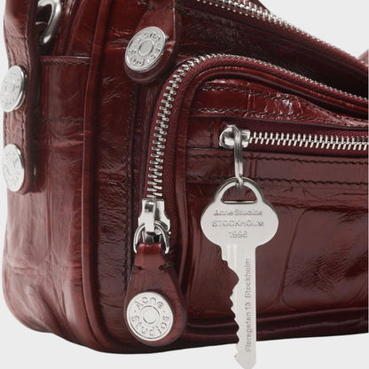 Tasoni burgundy patent croc-embossed calf leather shoulder bag with silver hardware and key charm.