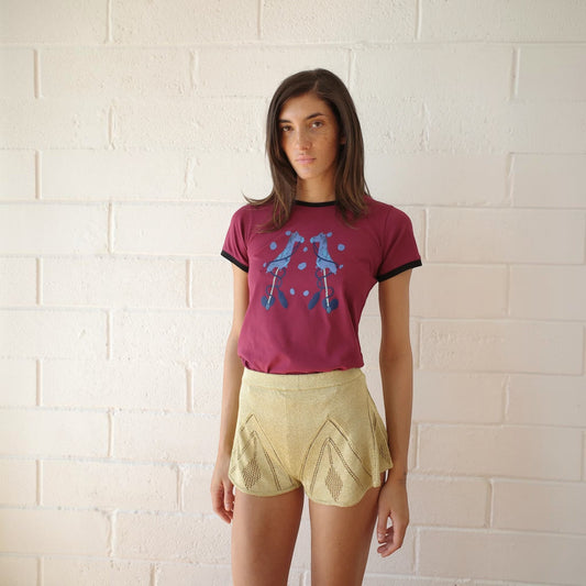 Model wearing Tasoni Conner Ives gold knitted pointelle godet shorts with a maroon graphic ringer t-shirt.
