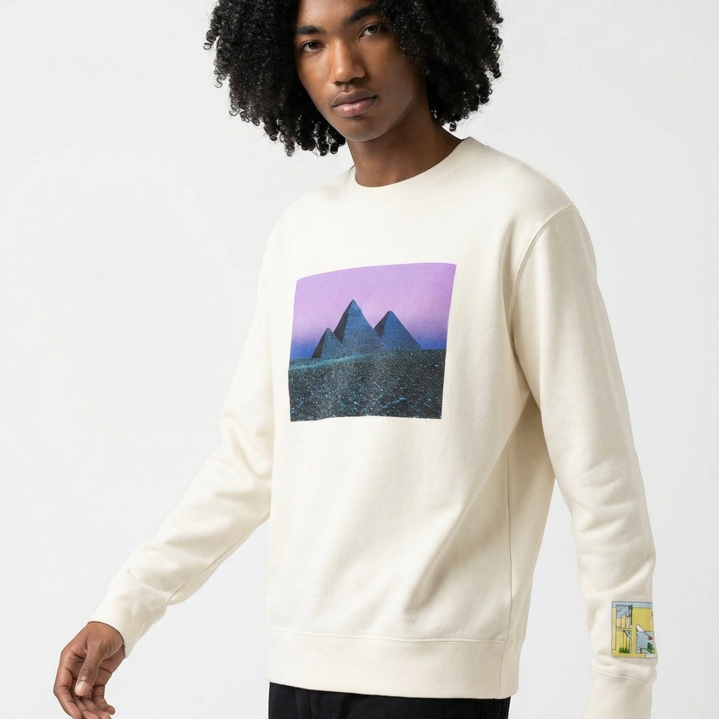 Tasoni cream cotton crew neck sweatshirt with a graphic print of pyramids under a purple sky on the front and a cartoon graphic on the sleeve.