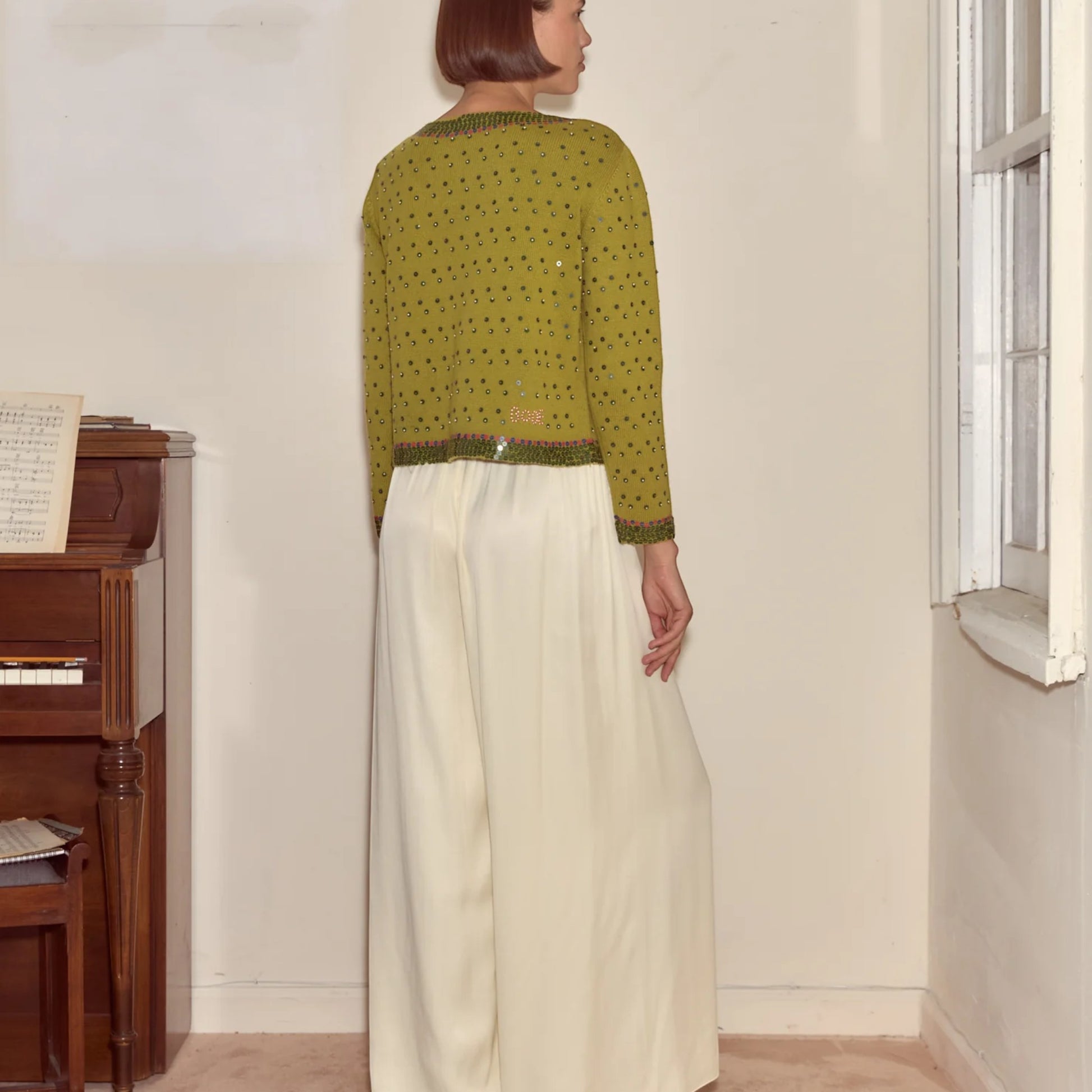Tasoni green knit cardigan with fairy floss sequins, crew neck, and beaded trim. Model wears cream wide-leg pants.