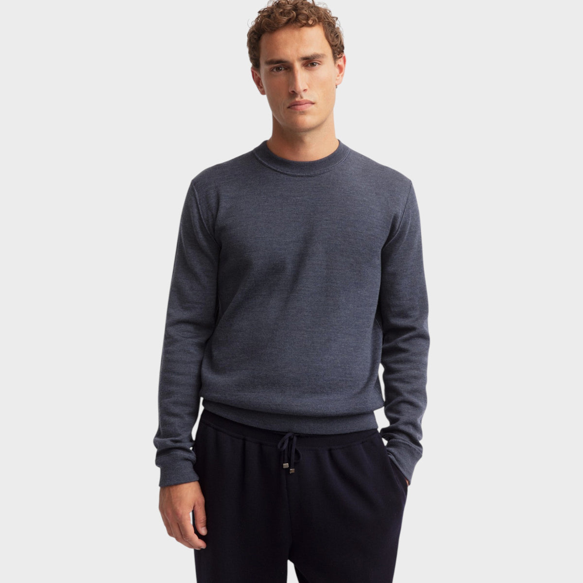 Male model wearing a Tasoni Iris von Arnim Dawson charcoal grey wool crewneck sweater with ribbed trim.