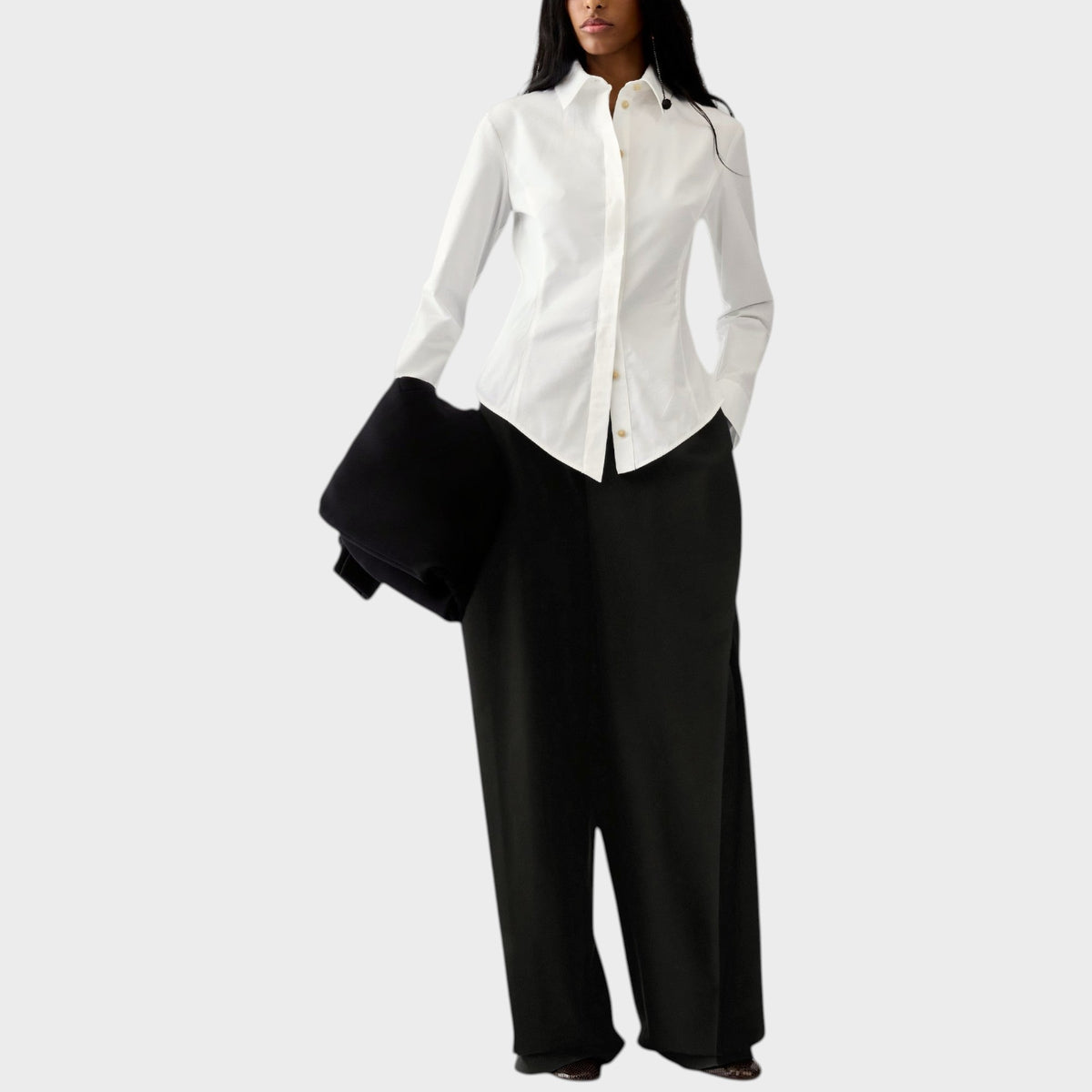 Tasoni model wearing a white Jacquemus cotton poplin asymmetric shirt with long cuffs and black wide-leg trousers.