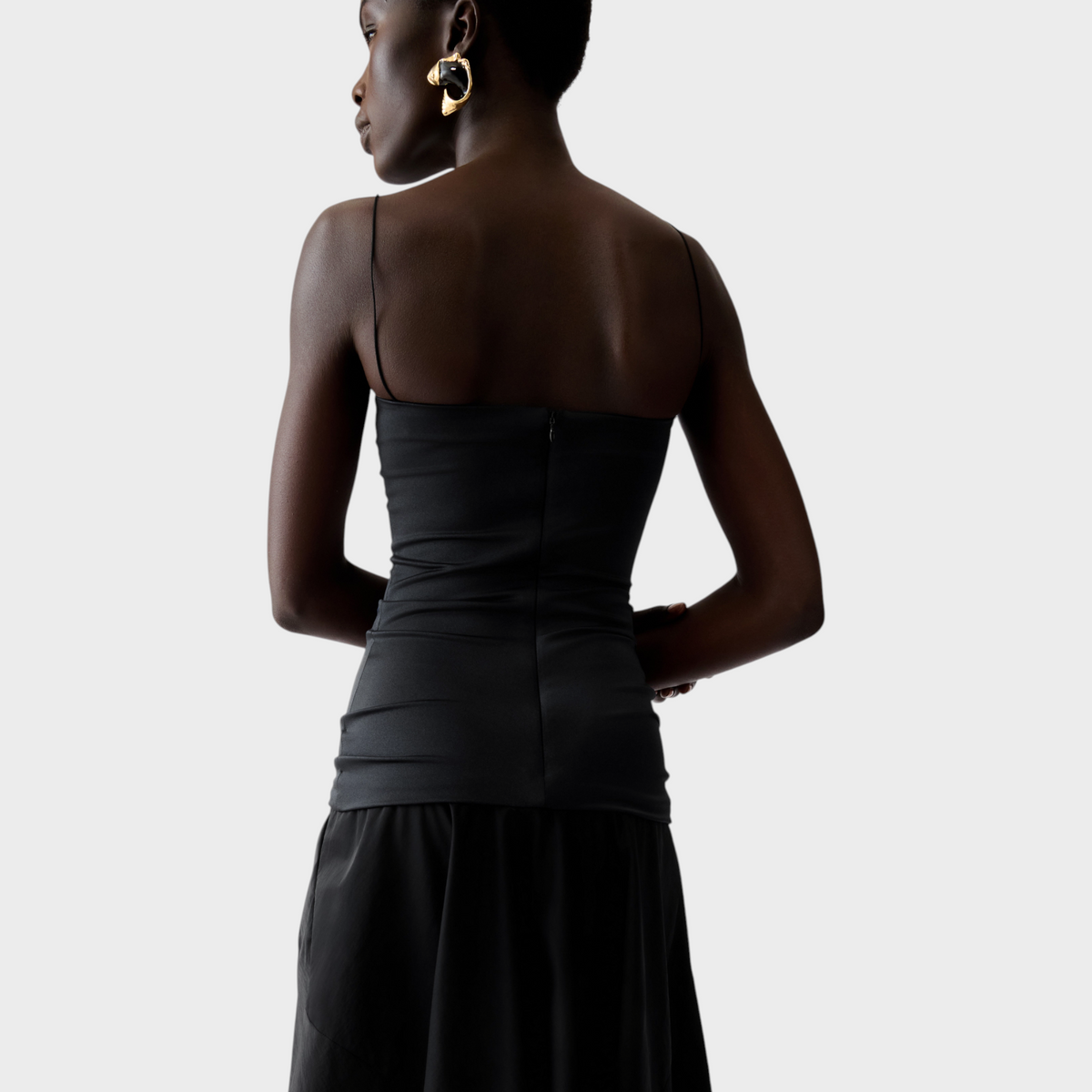 Model wearing a black Tasoni Jacquemus La Robe Paradiso midi dress with thin spaghetti straps and gold earrings