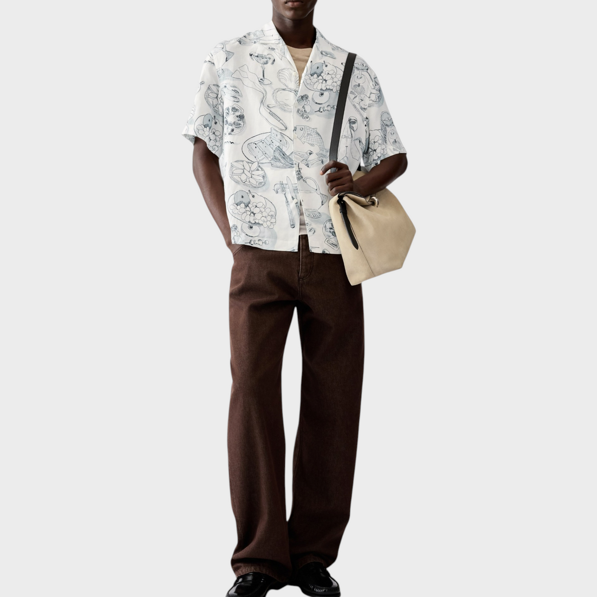 Tasoni model wearing a white Jacquemus La Chemise Cocktail shirt with blue graphic prints and brown trousers.