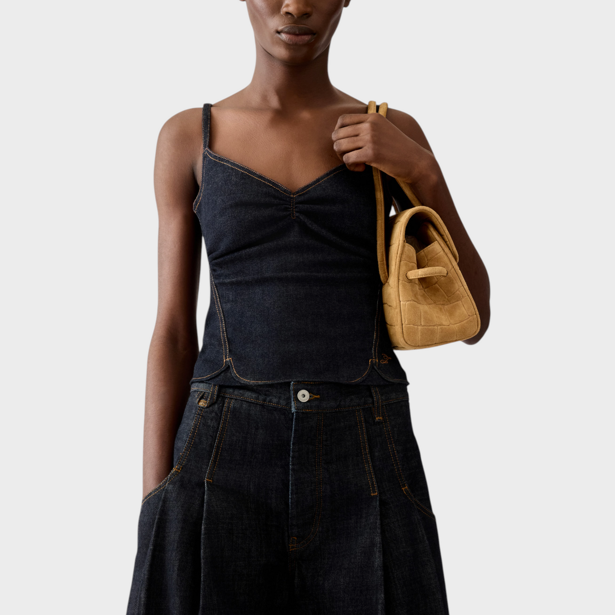 Tasoni model wearing a dark indigo denim Jacquemus Le Haut De-Nimes tank top with contrast stitching and a tan bag.