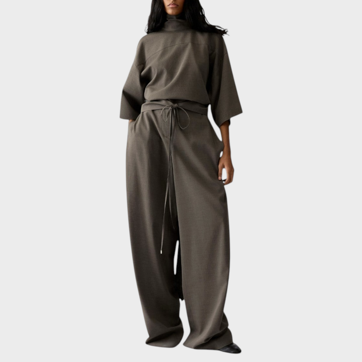 Tasoni model wearing a dark grey Jacquemus La Blouse Havana draped fluid top with matching high-waisted wide-leg trousers