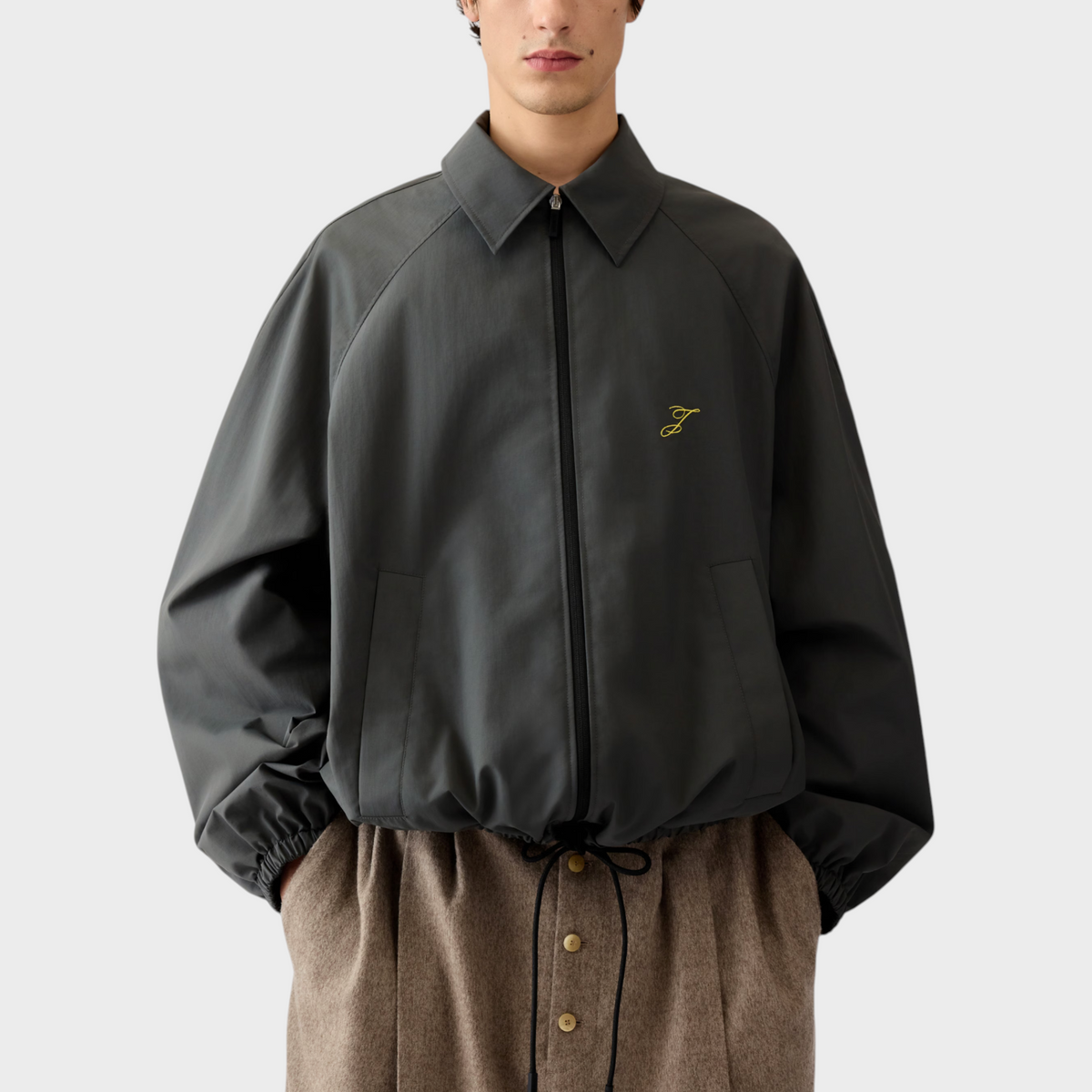 Tasoni Jacquemus Le Coupe-Vent wind breaker jacket in dark grey with a yellow logo and drawstring hem