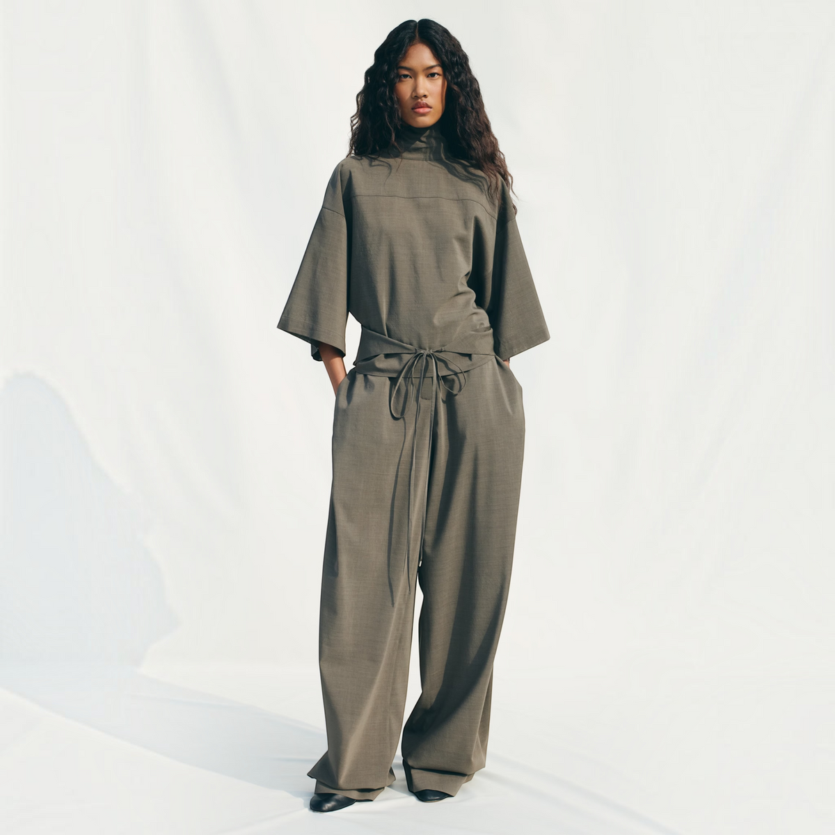 Model wearing Tasoni Jacquemus La Blouse Havana draped fluid top in olive green with matching wide-leg trousers