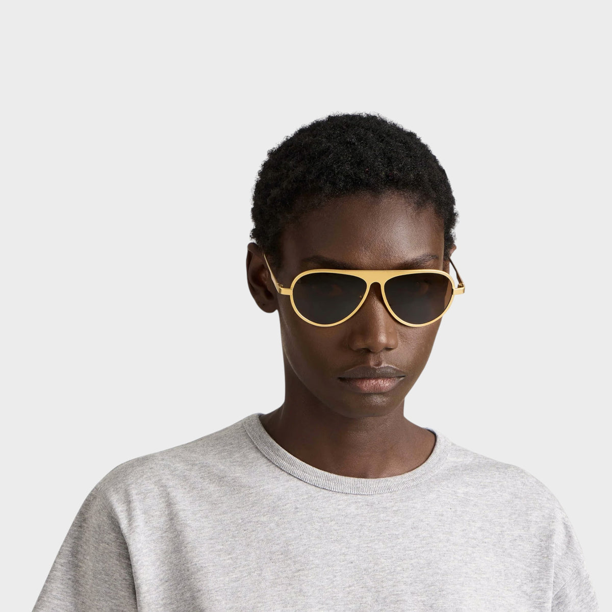 Model wearing Tasoni JW Anderson Jwa05 gold titanium aviator sunglasses with dark lenses against a white background.