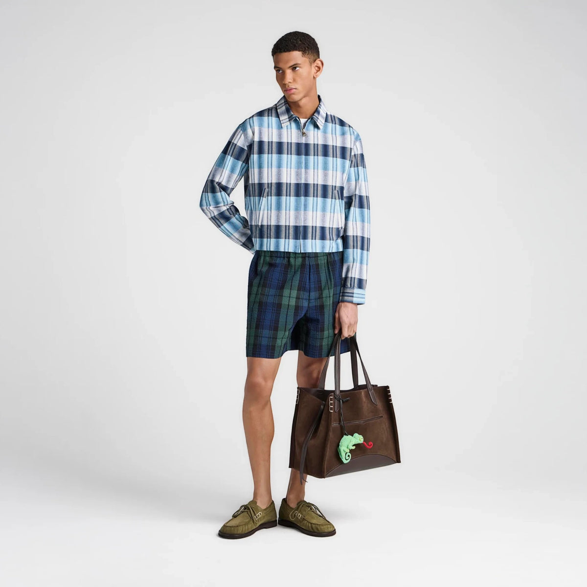 Male model wearing Tasoni JW Anderson blue and green plaid check shorts with a matching jacket and brown tote bag.