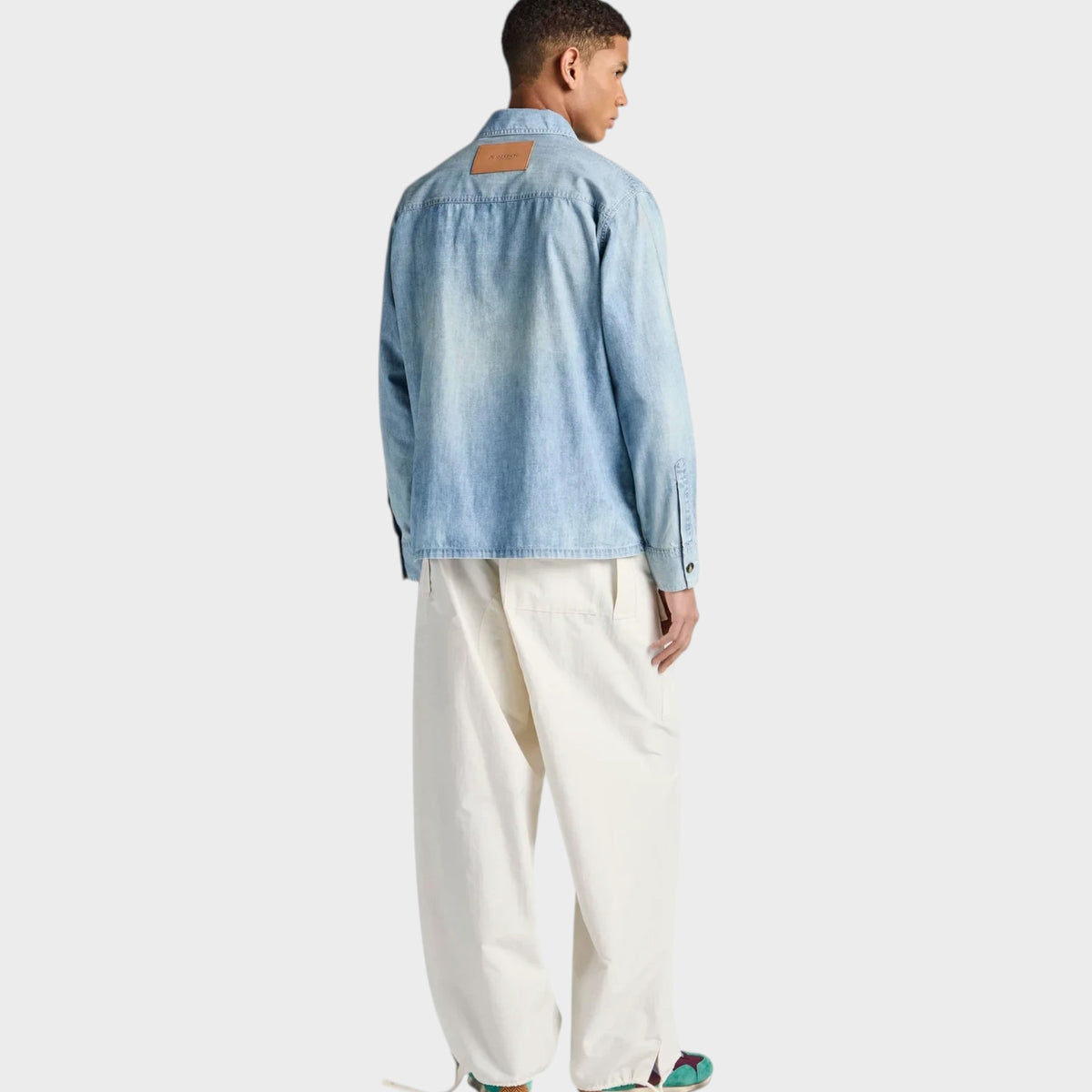 Model wearing a Tasoni J.W.Anderson pale blue cotton denim shirt with a tan leather back patch and loose white trousers