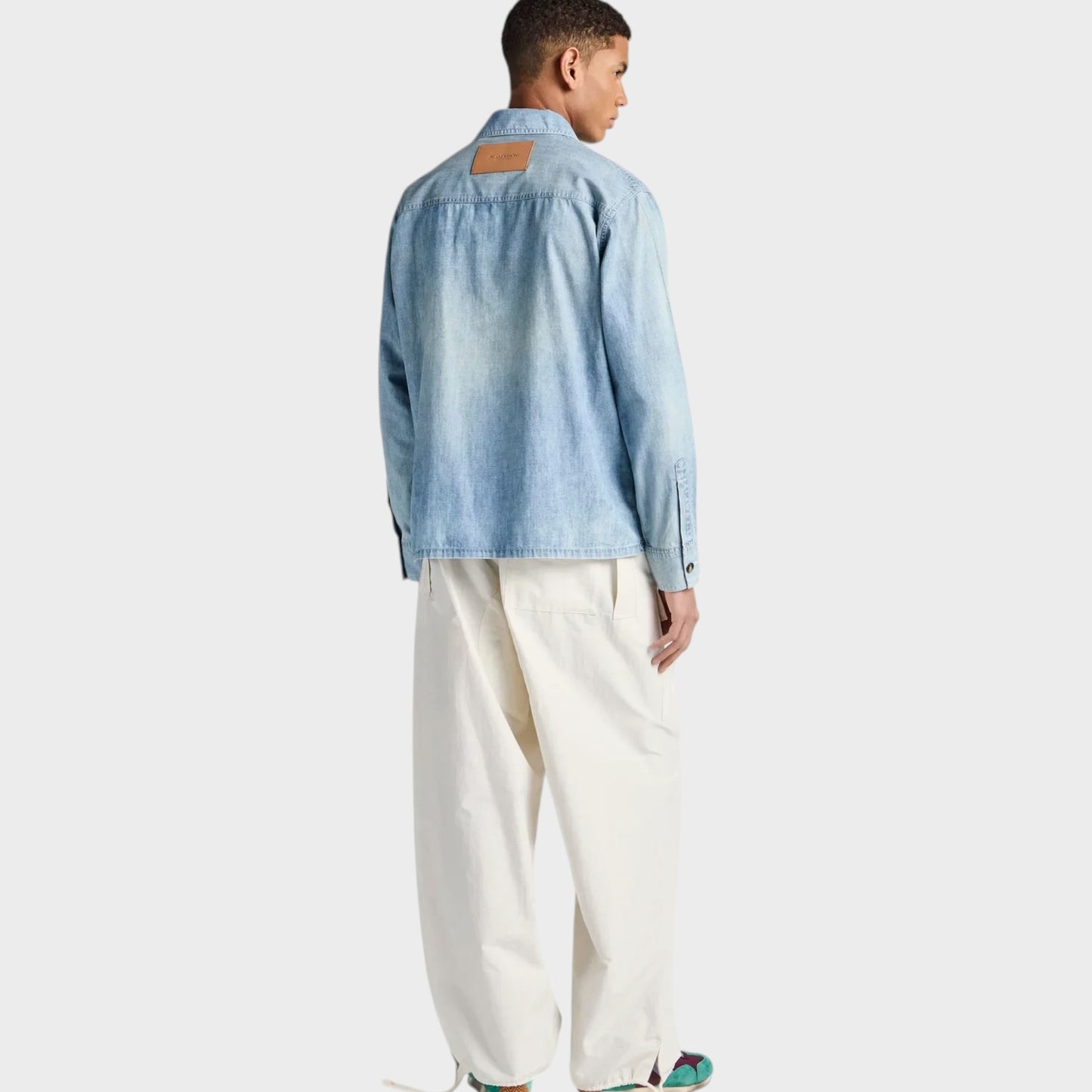 Model wearing a Tasoni J.W.Anderson pale blue cotton denim shirt with a tan leather back patch and loose white trousers