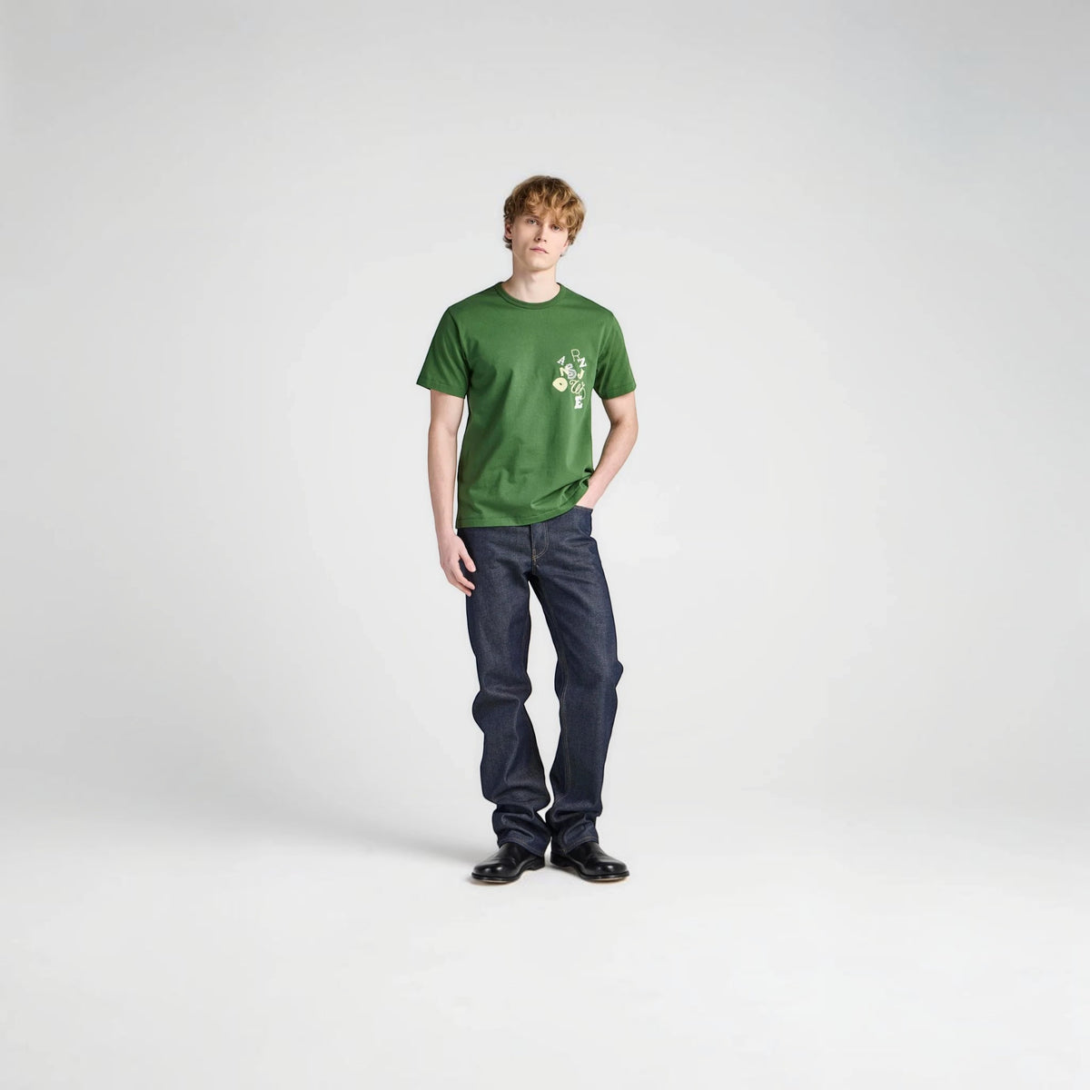 Male model wearing a green Tasoni JW Anderson cotton T-shirt with white embroidery and dark blue denim jeans.