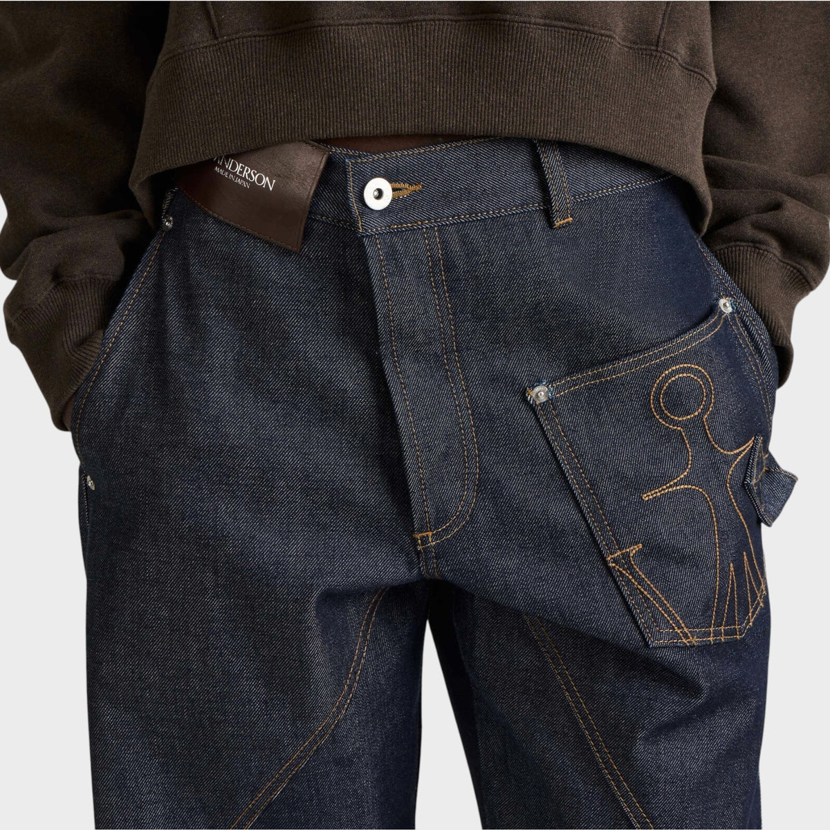 Tasoni JW Anderson dark blue denim workwear jeans featuring twisted seams and an anchor logo pocket detail.