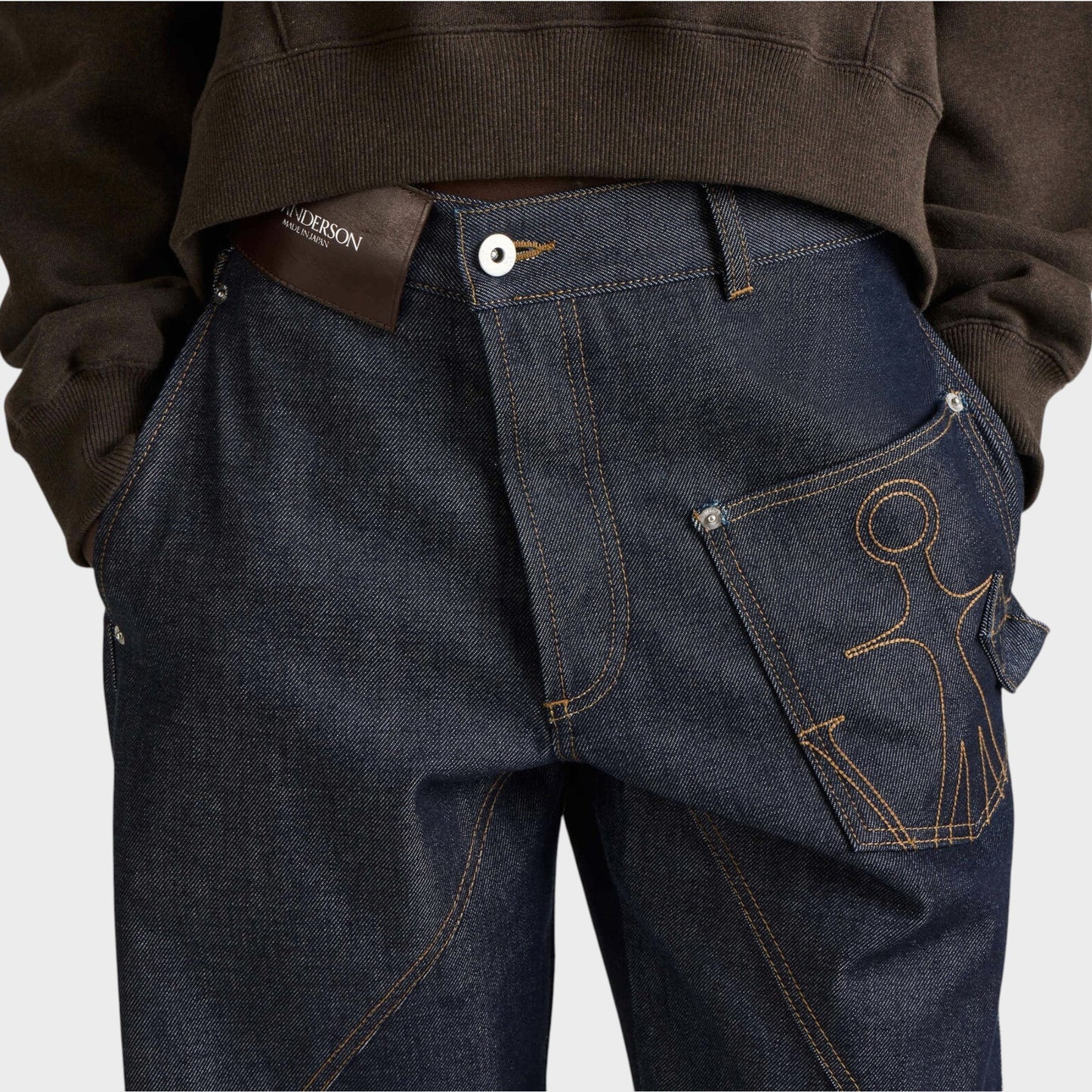 Tasoni JW Anderson dark blue denim workwear jeans featuring twisted seams and an anchor logo pocket detail.