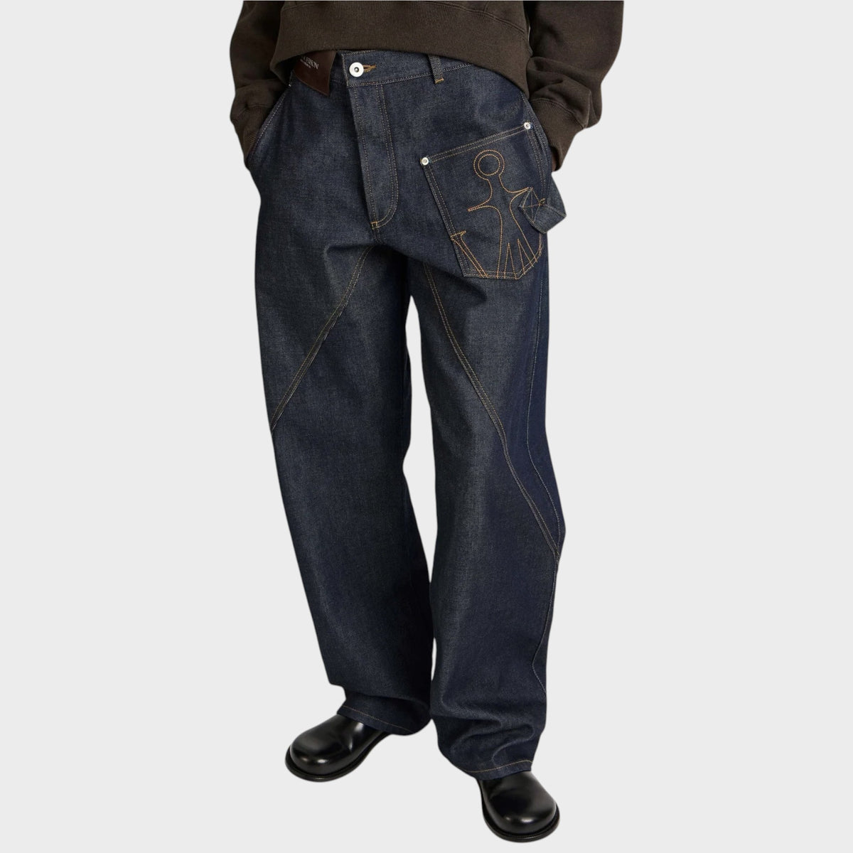 Tasoni JW Anderson dark indigo denim jeans with twisted workwear seams and embroidered pocket detail on model.