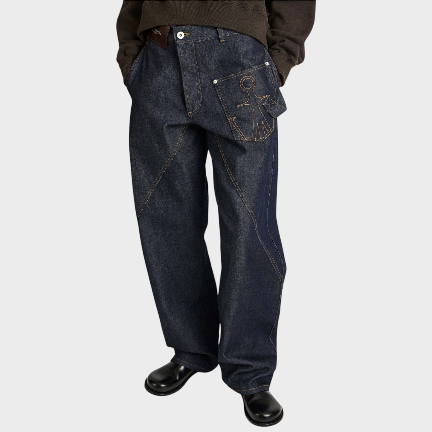 Tasoni JW Anderson dark indigo denim jeans with twisted workwear seams and embroidered pocket detail on model.