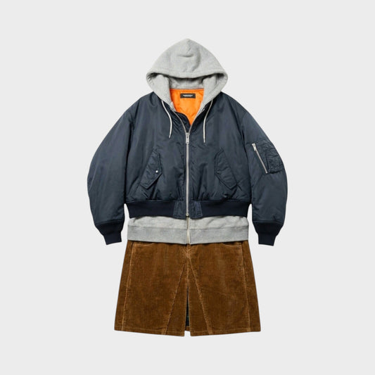 Tasoni navy blue bomber jacket with grey hood and orange lining, layered over a grey sweatshirt and brown corduroy skirt.