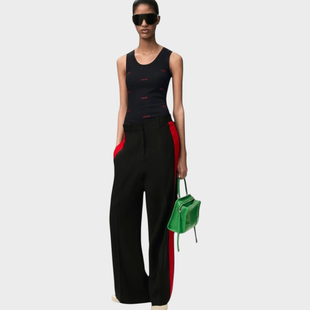 Model wearing a black Tasoni Loewe cotton tank top with red logo print, paired with black trousers and green bag.