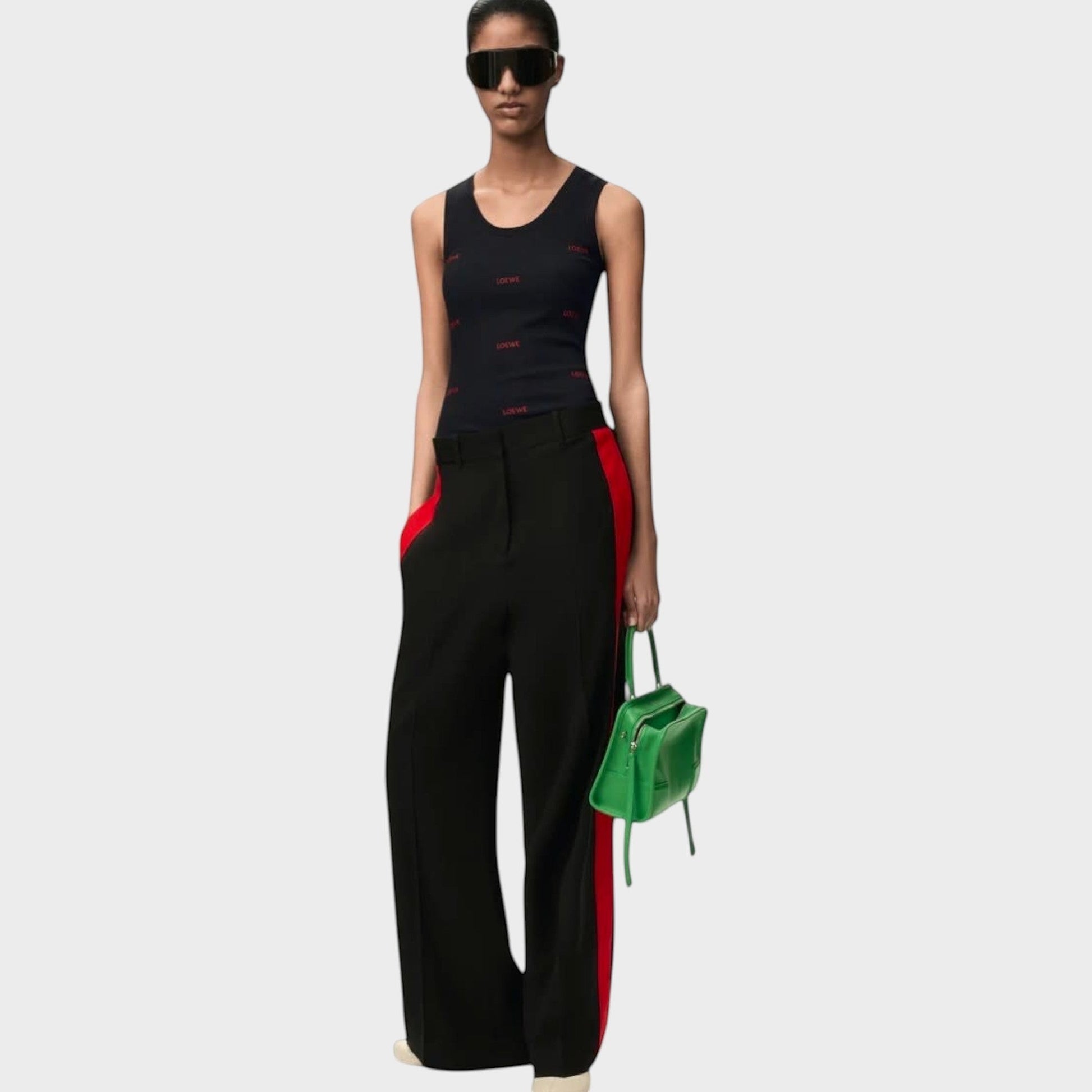 Model wearing a black Tasoni Loewe cotton tank top with red logo print, paired with black trousers and green bag.