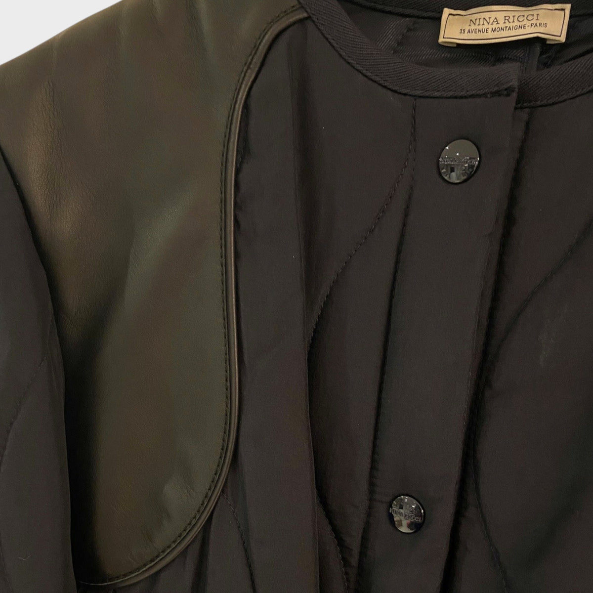 Tasoni Nina Ricci black quilted coat featuring smooth leather shoulder panels and branded button closures.