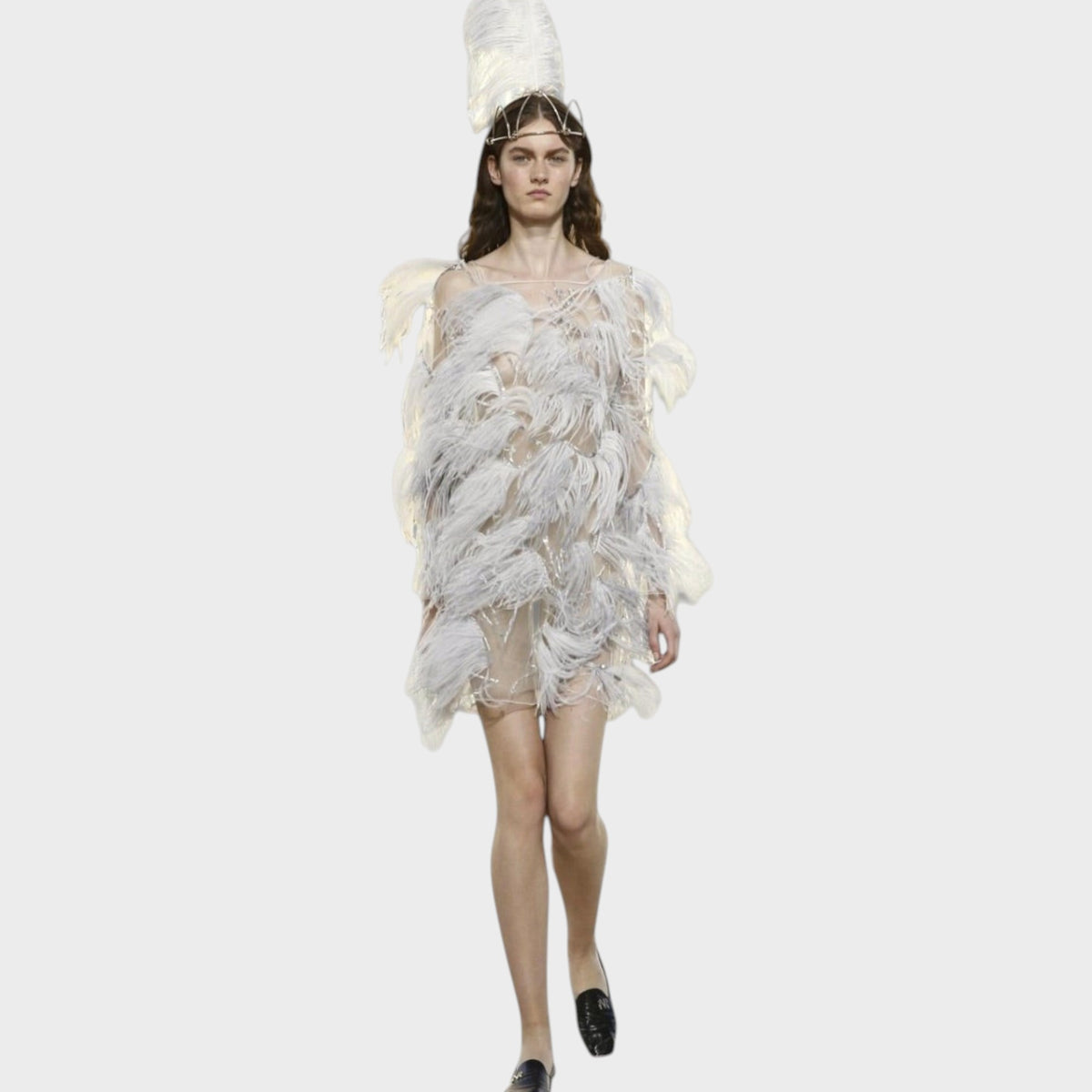 Model wearing a Tasoni Nina Ricci sheer mini dress covered in white feathers with a matching tall feather headpiece.