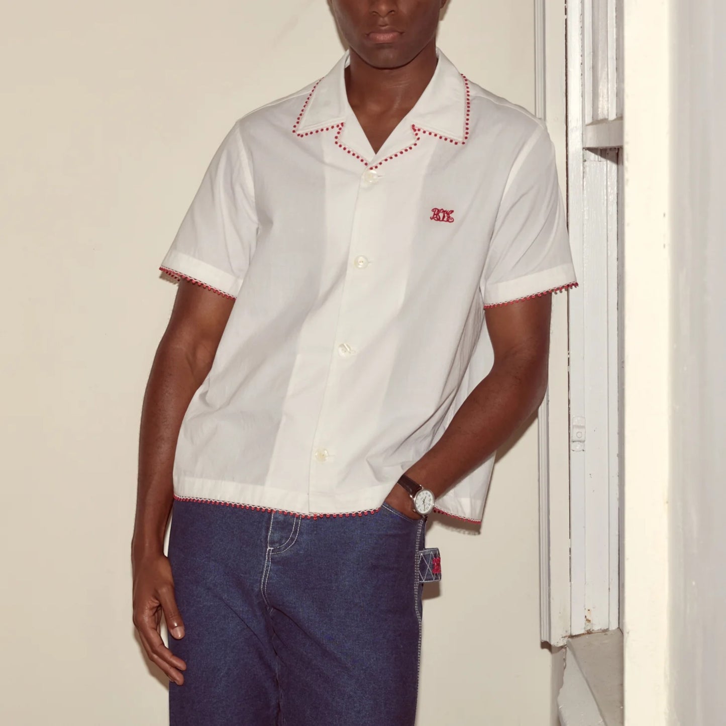Tasoni white short-sleeve button-up shirt with red trim and embroidered logo, paired with dark wash jeans.