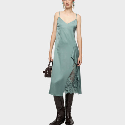 Tasoni sage green sleeveless slip midi dress with lace detail and V-neck. Model wears cowboy boots and holds a dark handbag.