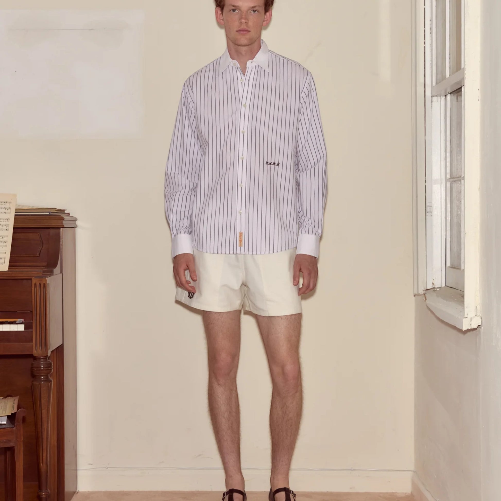 Tasoni Steamboat Stripe Shirt in black and cream cotton with embroidered logo detail. Model wears cream shorts and black shoes.