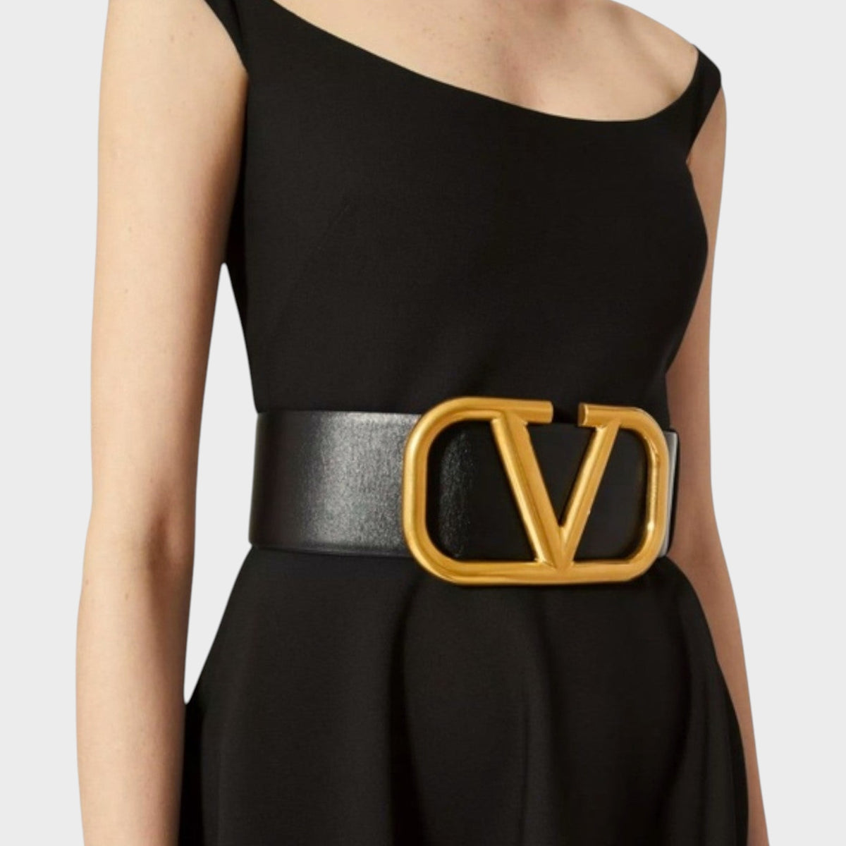 Tasoni Valentino black leather belt featuring a large gold-tone V logo buckle worn over a black dress