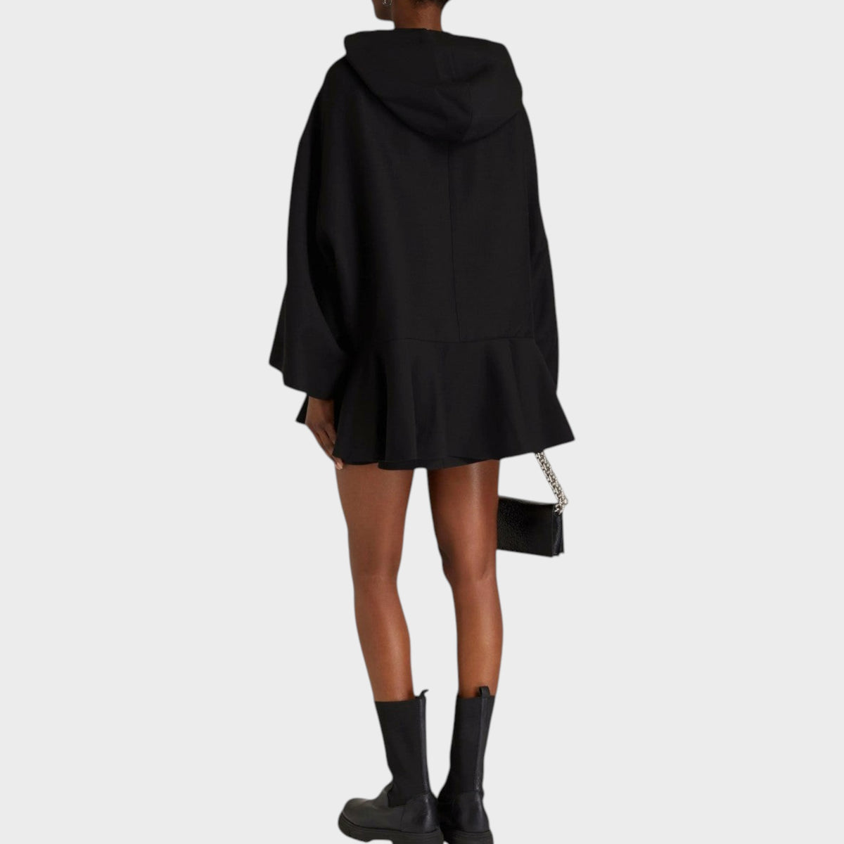 Back view of a model wearing a black Tasoni Valentino x Undercover wool and silk hooded mini dress with a peplum hem.